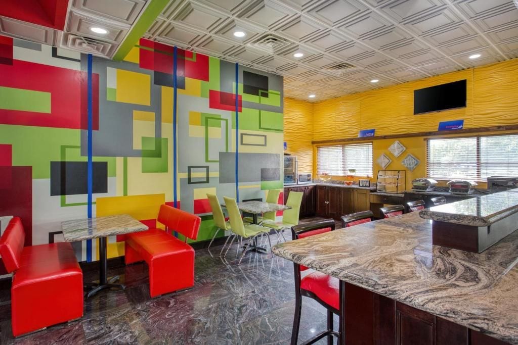 Un ristorante con un'originale parete decorata con motivi geometrici colorati, sedute rosse e verdi e un bancone in marmo.