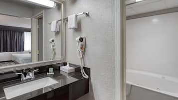 A hotel bathroom with a black sink, a mirror, a hairdryer, and a bathtub.