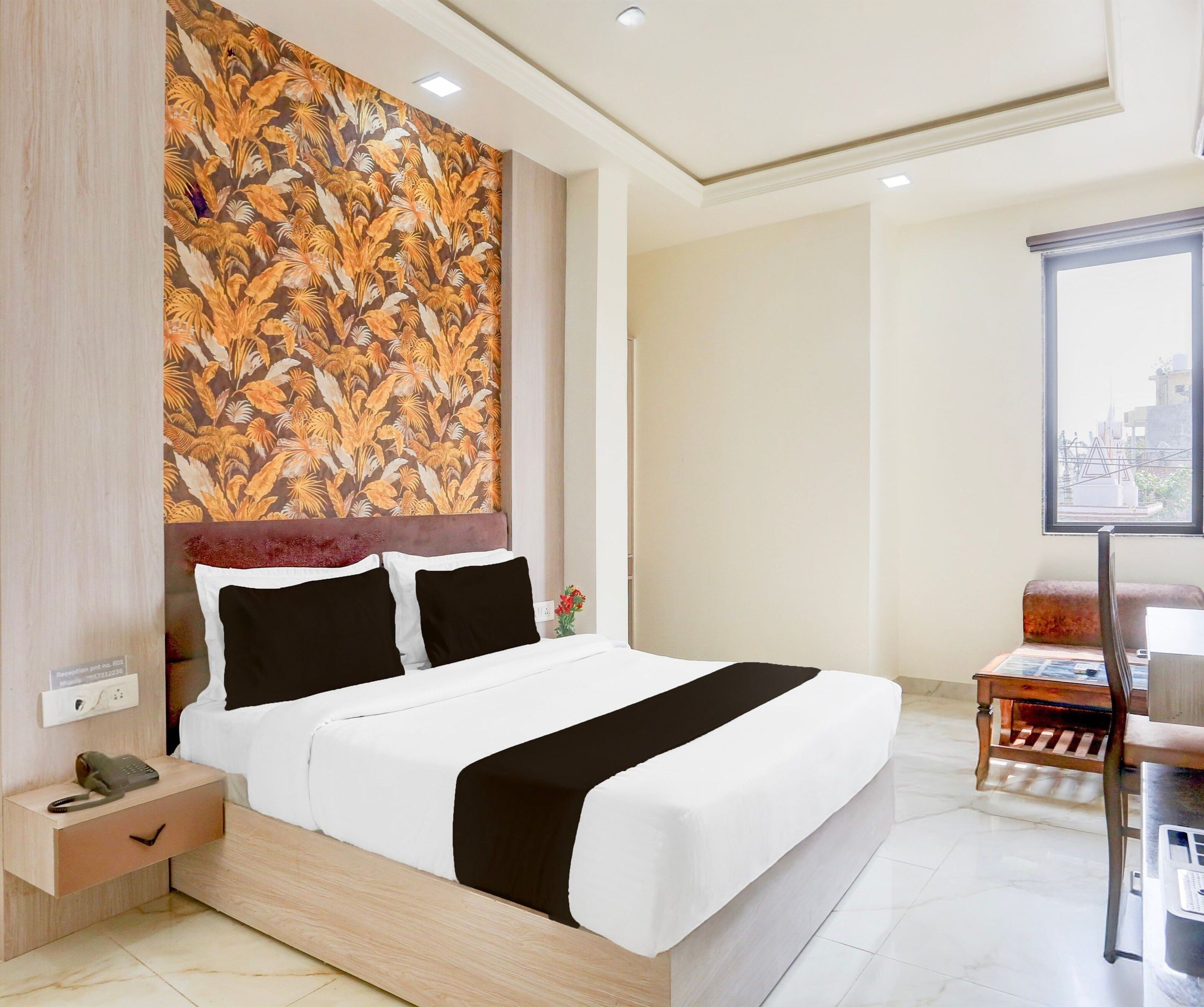 A hotel room with a bed, a nightstand, a desk, and a window with a city view.