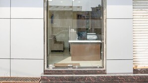 Ein moderner Gebäudeeingang mit Glastür, einem kleinen Podest davor und einem Metallgitter im unteren Bereich.