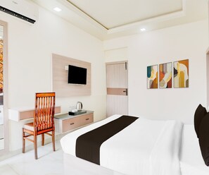 A hotel room with a bed, a desk, a chair, a television, and artwork on the wall.