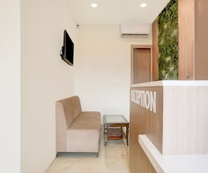 A reception area with a sofa, a small table, and a wall-mounted TV. - Deluxe Vidya Grand (Kichha)