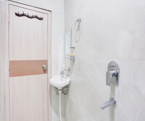 Een badkamer met een houten deur, een wit wastafelmeubel, een spiegel en een douche.