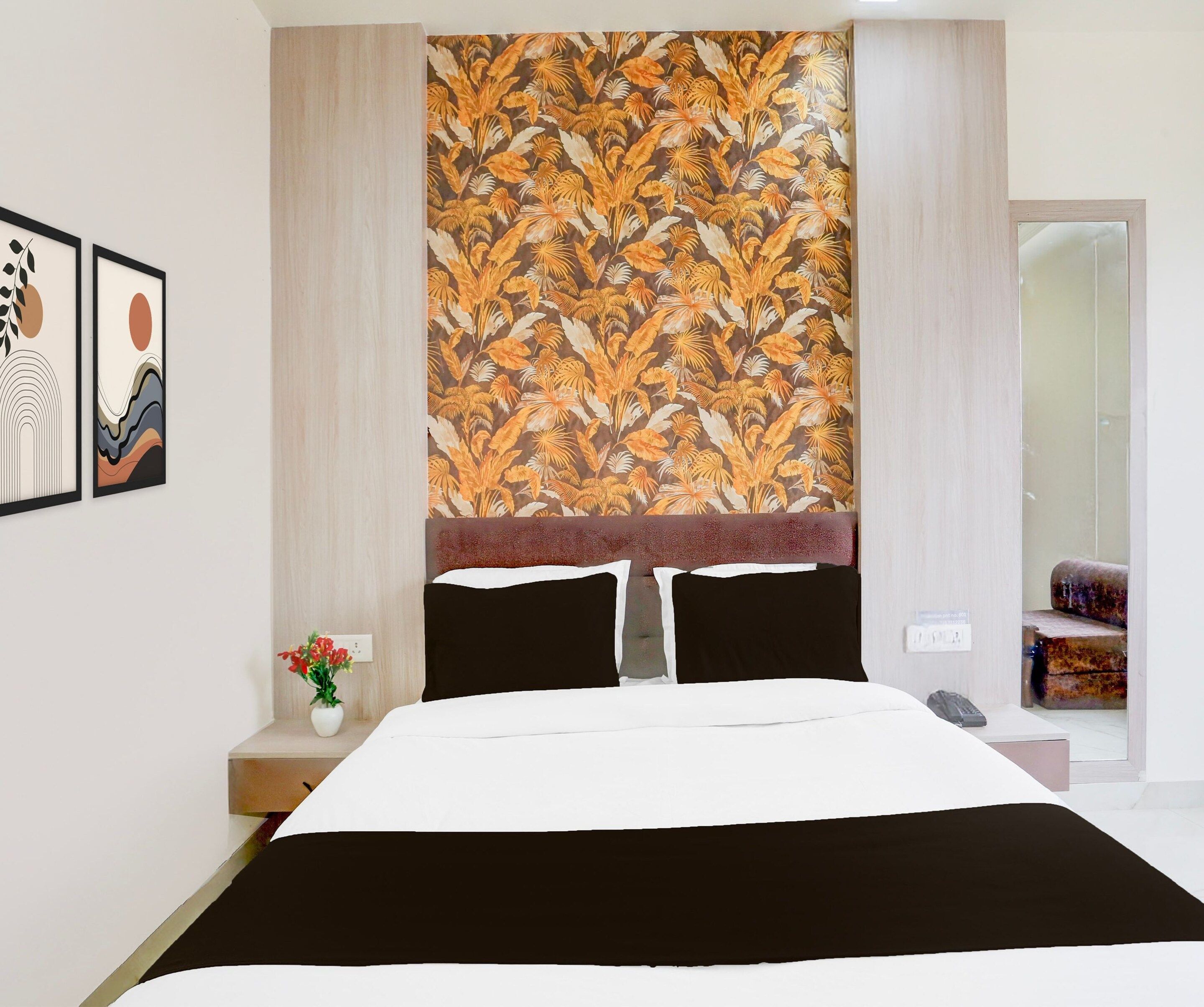 A bedroom with a bed, a nightstand with a vase of flowers, and a wall with a tropical leaf pattern.