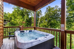 Un bain à remous sur une terrasse en bois, avec une balustrade en bois, entouré d’arbres.