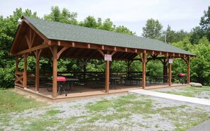 Un pavillon en bois doté de tables de pique-nique et d’un barbecue, entouré d’arbres.