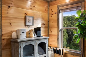 Ein Holzhaus-Interieur mit einer rustikalen Küchenarbeitsplatte, einer Kaffeemaschine, einem gerahmten Bild und einem Fenster mit Blick auf Grünflächen.