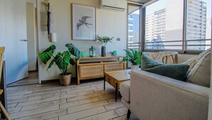 A modern living room with a sofa, a coffee table, a side table, a cabinet, and large green plants. - 2BR/2B Suite, A/C and heating, Parking (Estación Central)
