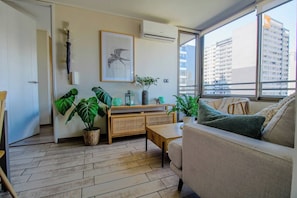 Un soggiorno moderno con un divano, un tavolino da caffè, un comodino, un mobile contenitore e piante verdi di grandi dimensioni.
