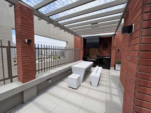 Een terras buiten met een pergola, zitplaatsen en een barbecuehoek.