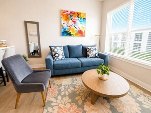 Een woonkamer met een bank, fauteuil, salontafel en een kleurrijk abstract schilderij aan de muur.