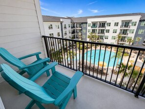Ein Balkon mit zwei türkisblauen Stühlen, einem Pool und einem Gebäudekomplex im Hintergrund.