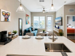 Eine moderne Küche mit Kochinsel, Essbereich und Wohnbereich inklusive Sofa und Couchtisch.