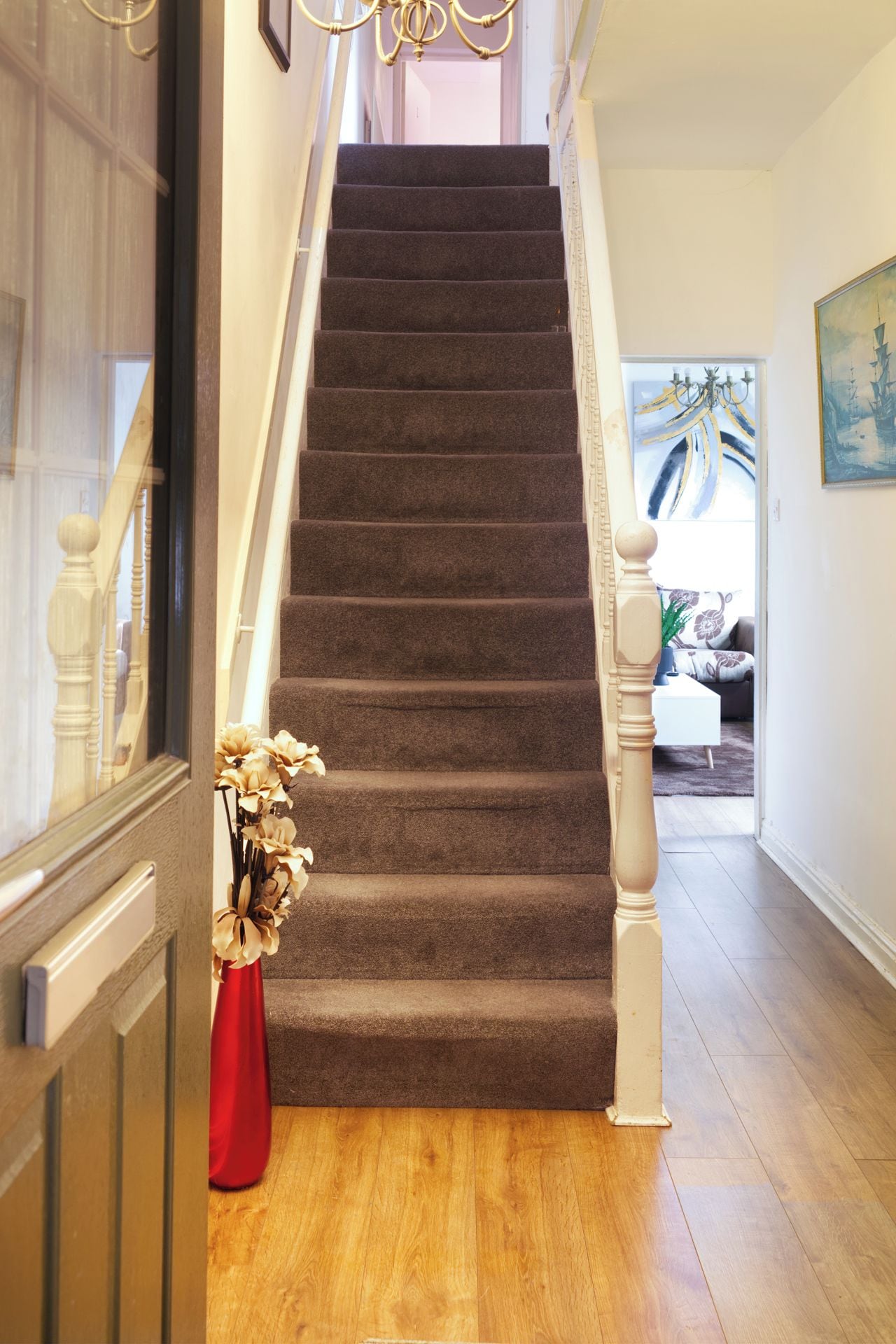 A staircase with carpeted steps, wooden balusters, and a red vase with dried flowers.