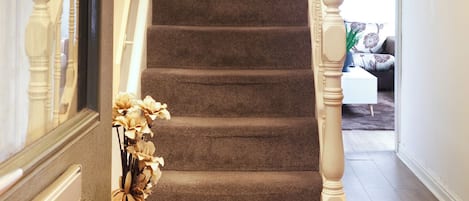 A staircase with carpeted steps, wooden balusters, and a red vase with dried flowers.