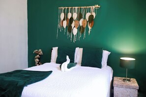 Ein Bett mit weißer Bettwäsche, einer grünen Wand und einem Wandbehang aus Makramee.