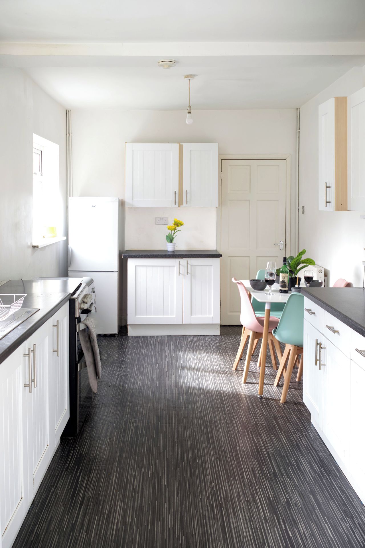 A modern kitchen with white cabinetry, a dining area with a table and chairs, and a dark wood floor.