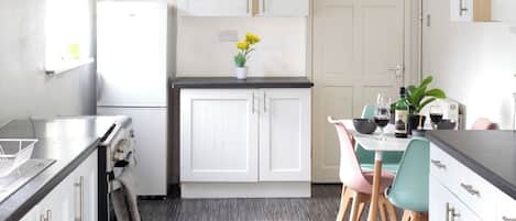 Une cuisine moderne avec des meubles blancs, un coin repas comprenant une table et des chaises, et un plancher en bois foncé.