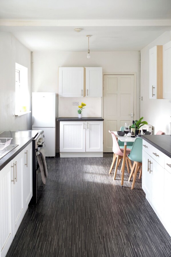 A modern kitchen with white cabinetry, a dining area with a table and chairs, and a dark wood floor.