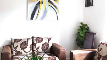 A living room with a brown leather sofa, a patterned armchair, a potted plant, and a chandelier.