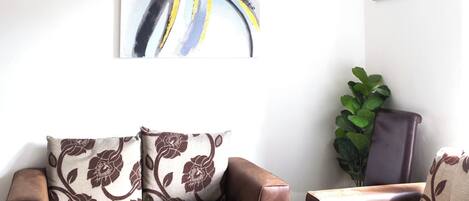 A living room with a brown leather sofa, a patterned armchair, a potted plant, and a chandelier.