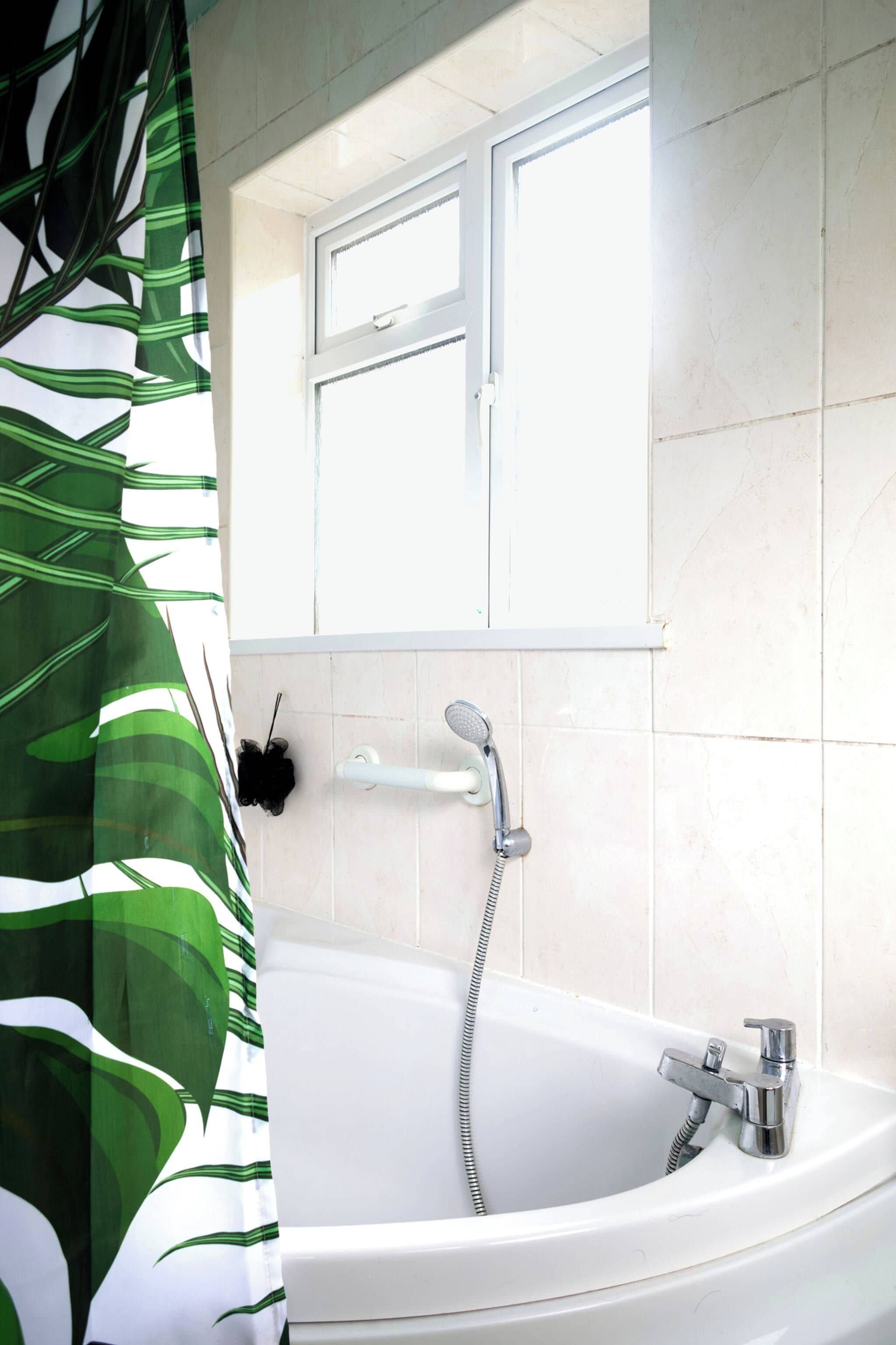 Ein Badezimmer mit Badewanne, Dusche, Fenster und Vorhang.