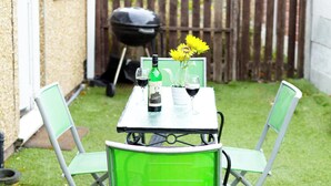 Une petite terrasse avec une table et des chaises, un barbecue et une clôture en bois en arrière-plan.