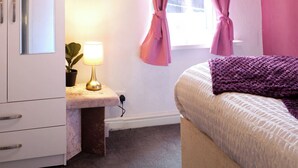 Une chambre à coucher avec un lit, un bureau avec une lampe, une armoire et des rideaux roses.