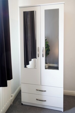 A white wardrobe with a mirrored door and a plant inside.