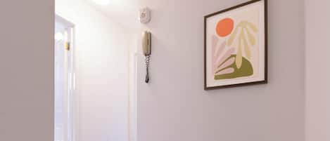 A hallway with a door, a wall-mounted telephone, and a framed abstract painting.