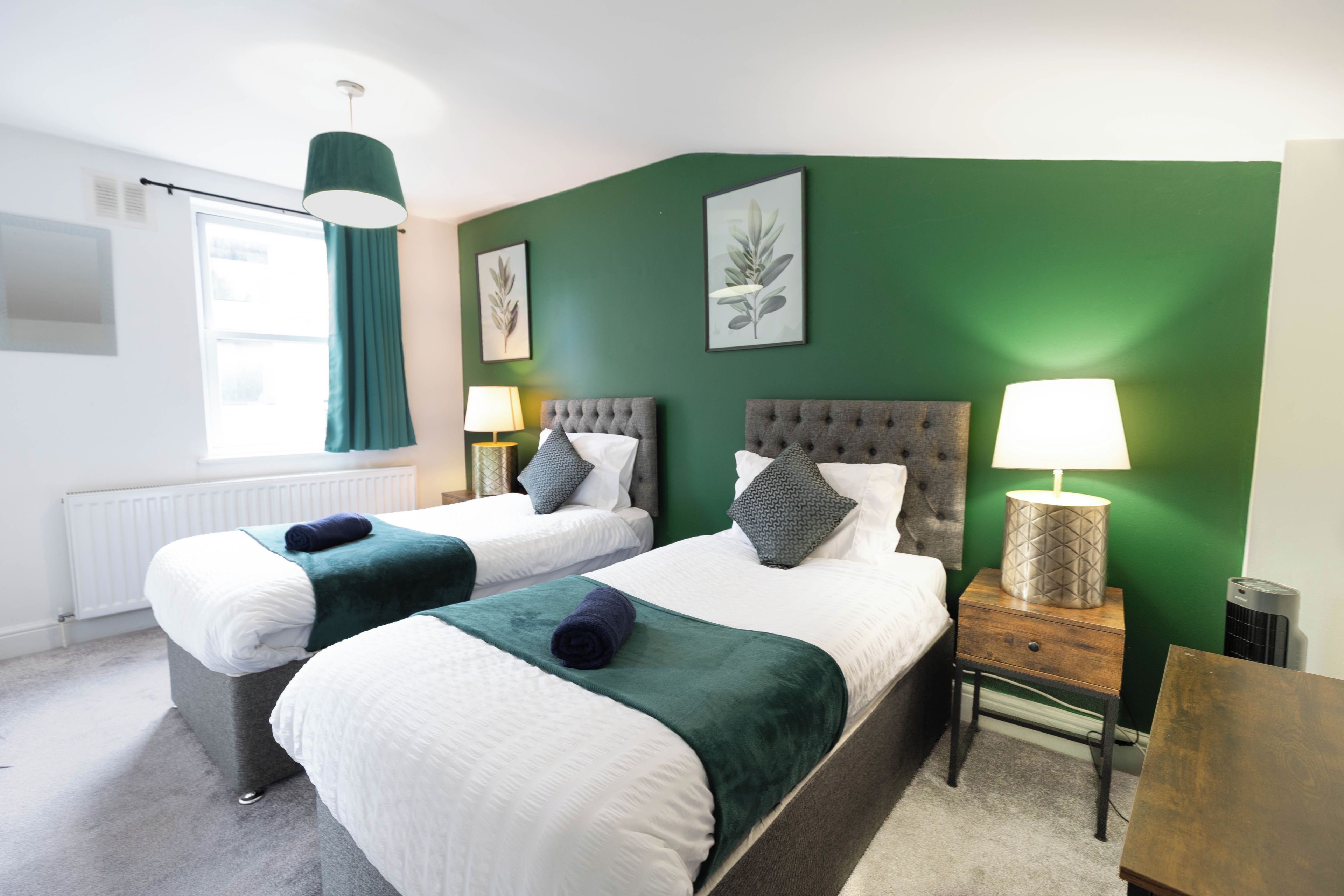 A hotel room with two beds, green walls, and a window with curtains.
