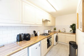 A modern kitchen with white cabinets, a wooden countertop, a coffee maker, a microwave, a stove, and a washing machine. - 2/3 Bedroom Duplex House, 2-minute walk from Camden Town tube Station, Sleeps 6 (London)