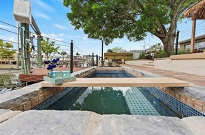 Ein Schwimmbecken mit Holzterrasse, umgeben von einer Steinmauer und einem großen Baum.