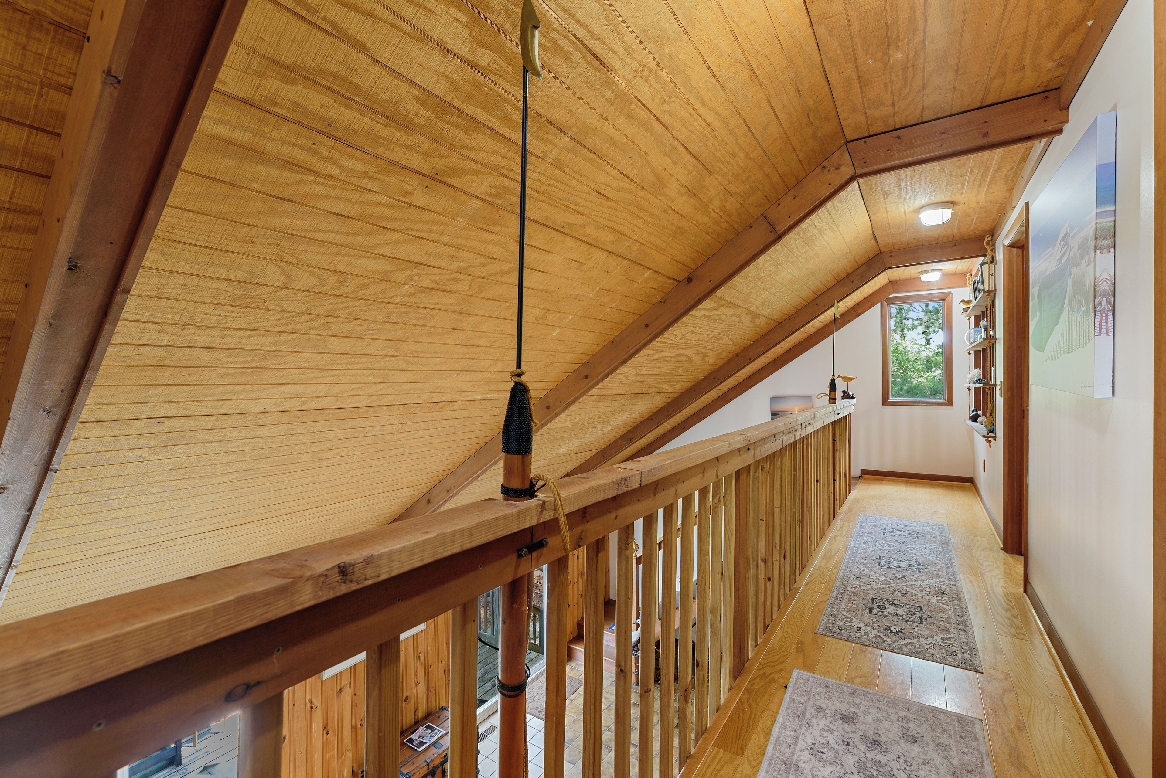 A wooden interior with a sloped ceiling, a wooden railing, and a view of the outside through a window.