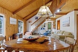 A wooden interior with a dining table, chairs, a staircase, and a sofa. - Villa Annick | Affordable Waterfront Retreat in Oyster Bay I (Chincoteague Island)