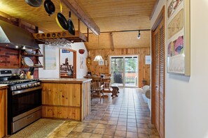 A kitchen with a central island, wooden cabinets, a stove, and hanging cookware. - Villa Annick | Affordable Waterfront Retreat in Oyster Bay I (Chincoteague Island)