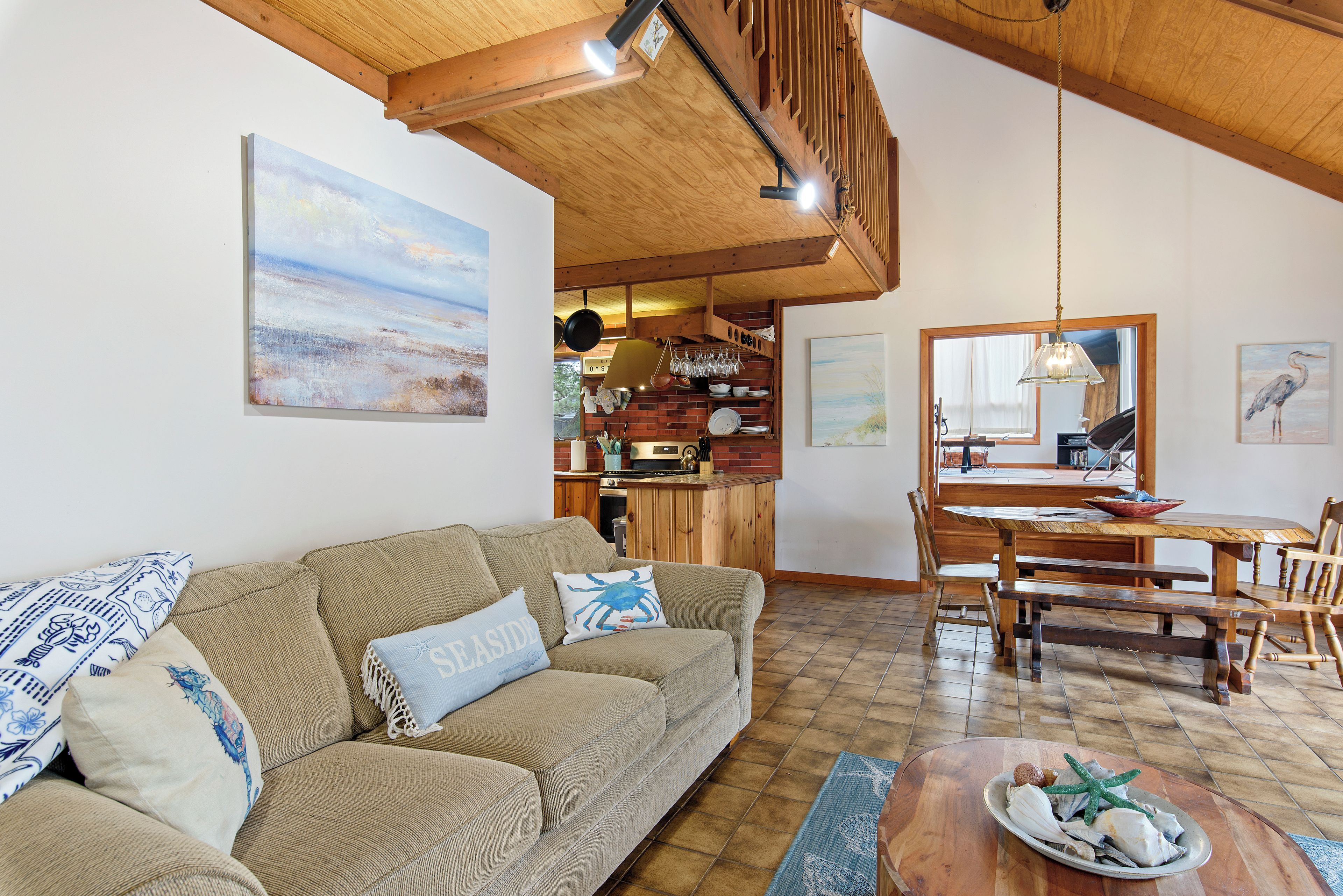 A cozy living room with a sofa, a dining table, and a kitchen area with a brick wall and wooden beams.