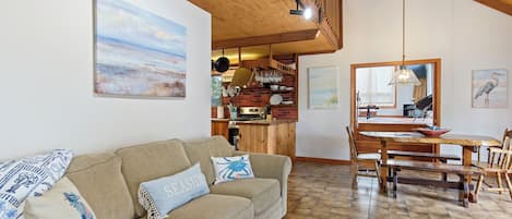 A cozy living room with a sofa, a dining table, and a kitchen area with a brick wall and wooden beams.