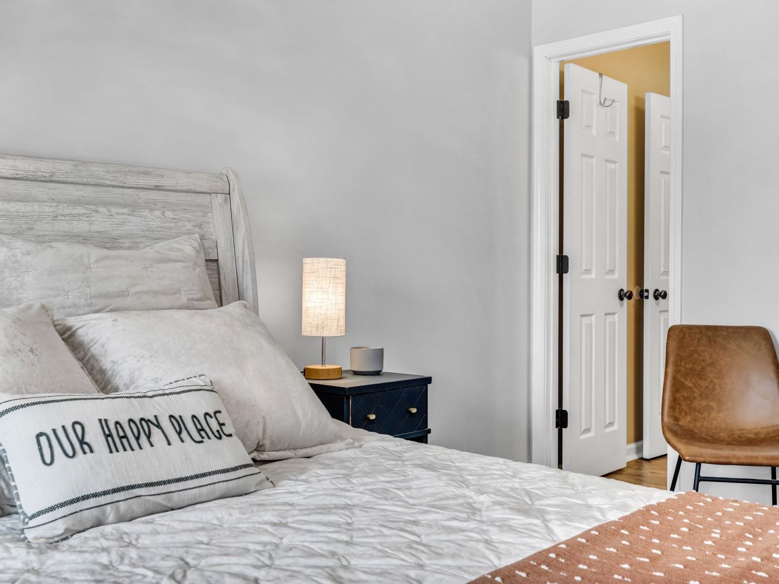 A bedroom with a bed, a bedside table with a lamp, a chair, and a door.