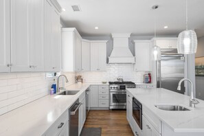 Eine moderne Küche mit weißen Schränken, einem Edelstahlkühlschrank, einem eingebauten Backofen und einer großen Kochinsel mit Spüle.
