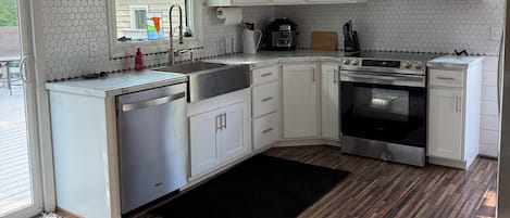 Una cocina con gabinetes blancos, estufa de acero inoxidable, horno empotrado, cafetera y ventilador de techo.
