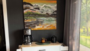 Une petite cuisine équipée d’une machine à café, d’une tasse et d’un tableau représentant un paysage de montagne.