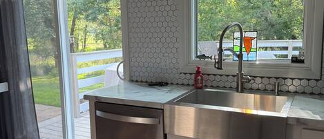 A kitchen with a stainless steel sink, a dishwasher, and a window with a view of greenery.