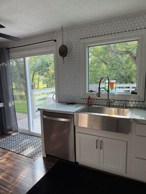 A kitchen with a stainless steel sink, a dishwasher, and a window with a view of greenery.