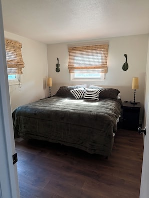 Quarto com cama, duas luminárias de cabeceira, janela com persianas e uma guitarra pendurada na parede.