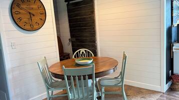 A dining area with a wooden table, four chairs, a wall clock, and a ceiling light fixture.