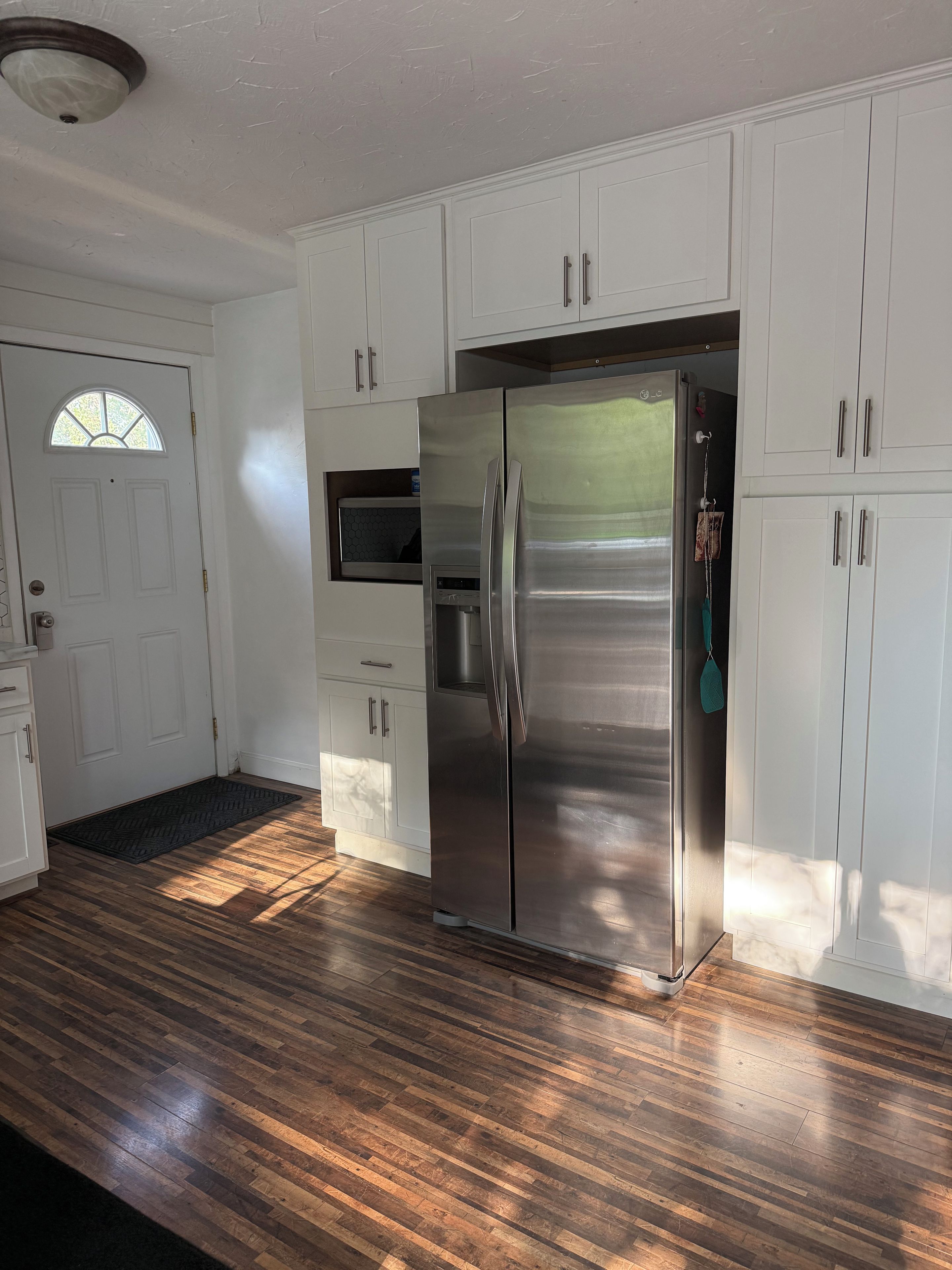 A kitchen with white cabinets, a stainless steel refrigerator, and a microwave.
