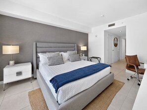 A modern bedroom with a large bed, bedside tables, a chair, and a walk-in closet. - Tiffany Celeste - Walk to Beach, Water Views, Rooftop Pool (Fort Lauderdale)