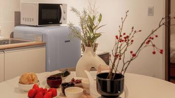 A modern kitchen with a microwave, a blue appliance, and a dining table set with food and a vase.