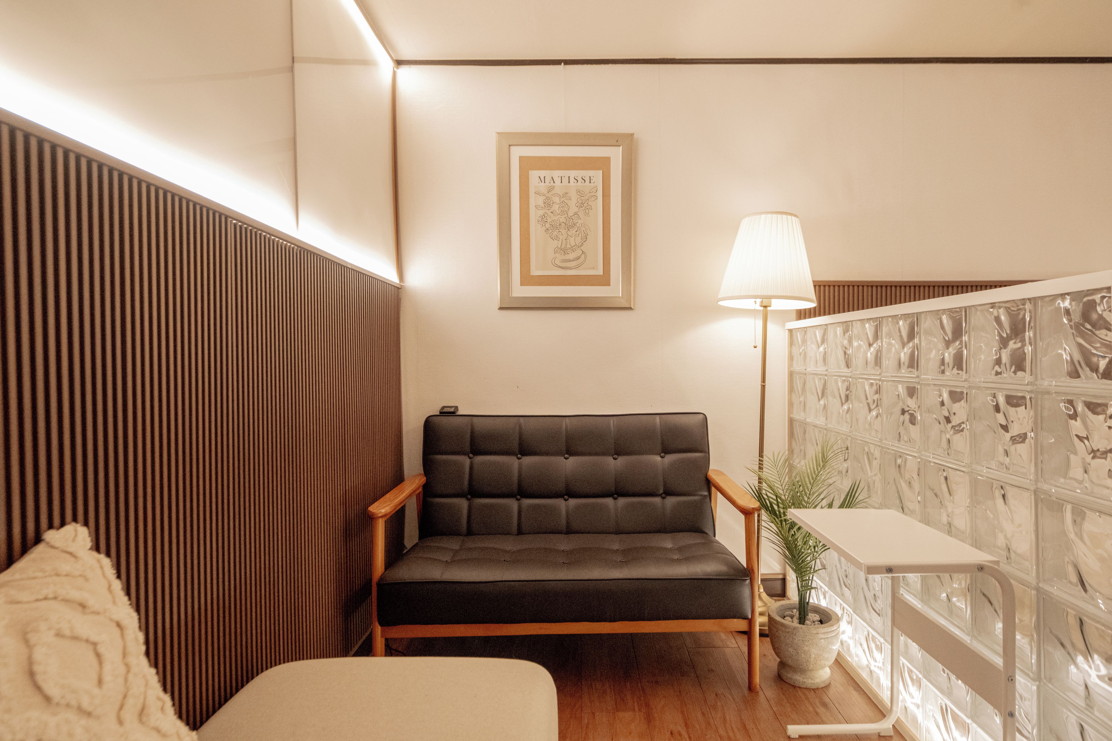 A modern living room with a dark leather sofa, a wooden side table, a lamp, and a framed artwork on the wall.